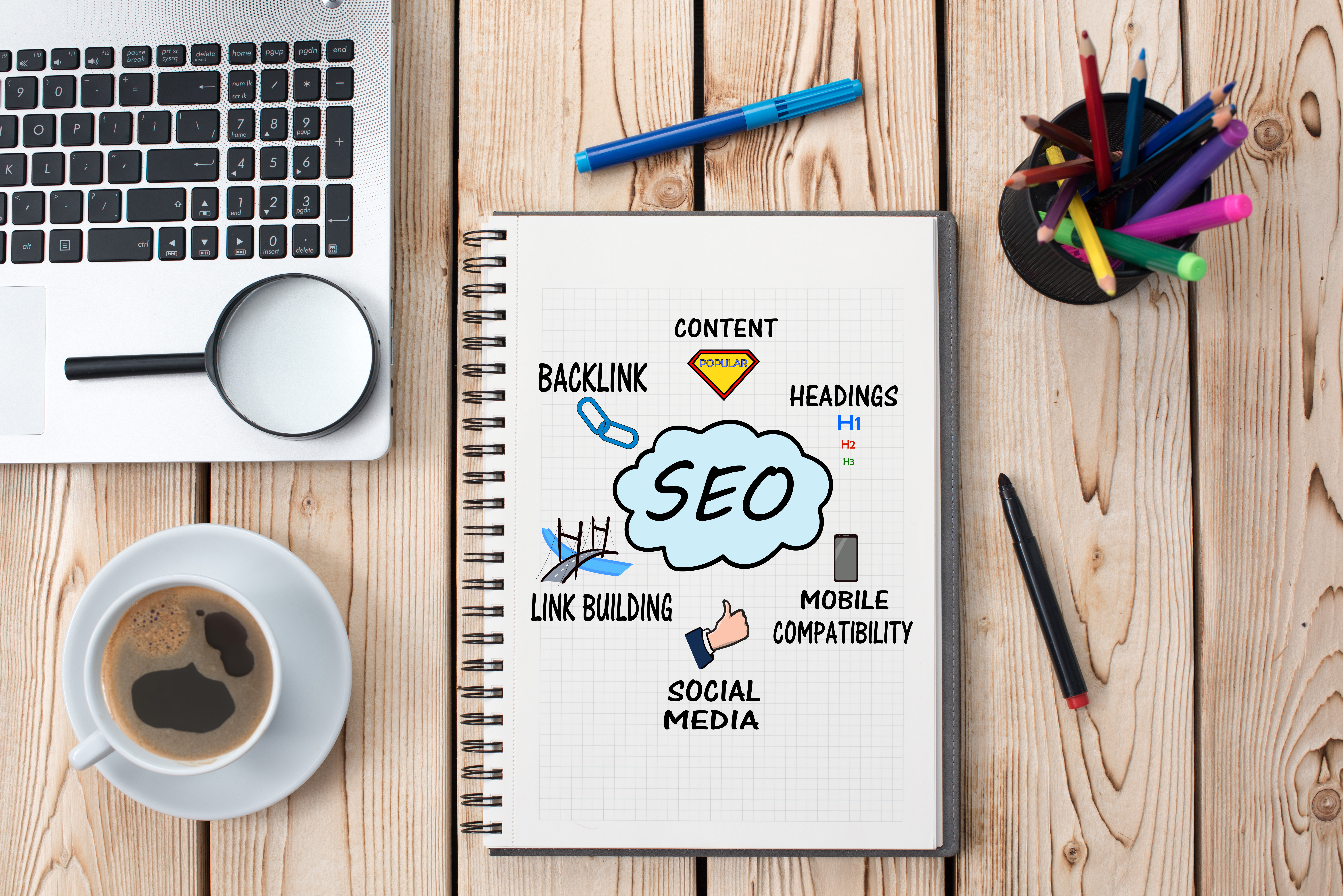 SEO infographic on notebook in workspace, infographic connects backlink, content, headings, link building, social media, and mobile compatibility to SEO in center